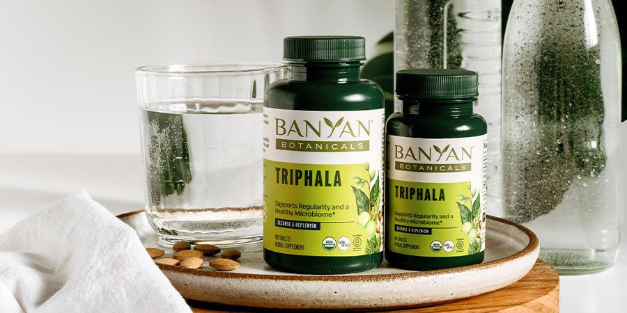 triphala tablets in large and small bottle next to glass of water