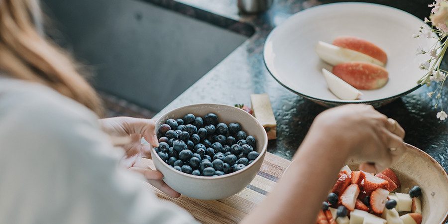 woman putting blueberries in fruit bowl