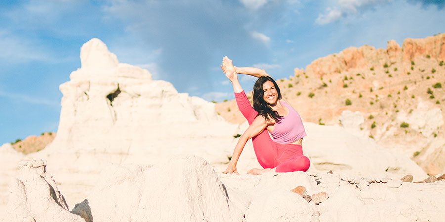 Banyan content writer and customer care specialist Seren practices compass pose on a rocky desert canyon in Albuquerque